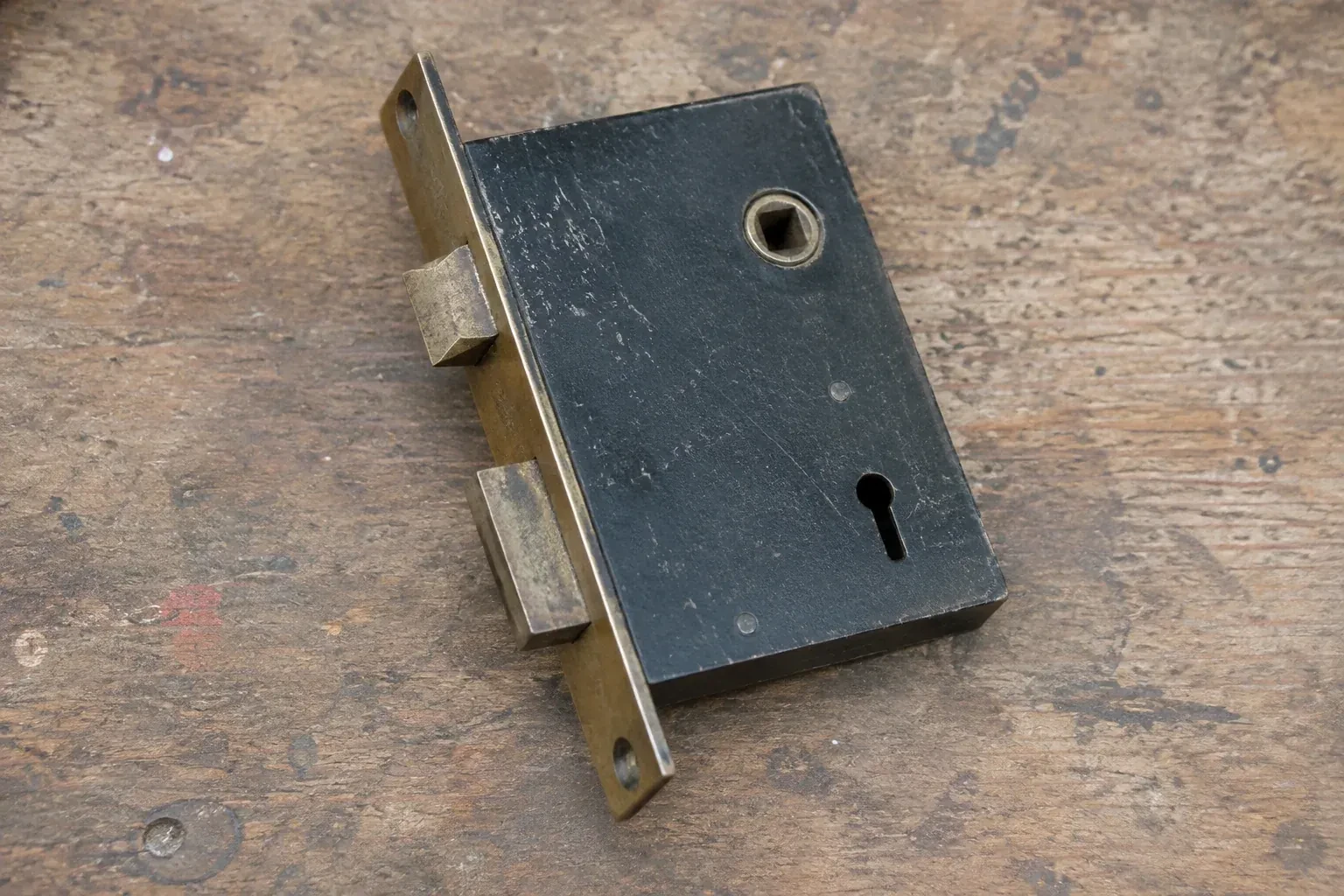 Closed mortise lock case with spindle opening, keyhole, latch and deadbolt on a wooden workbench. — Vintage Mortise Lock Service, Brantford