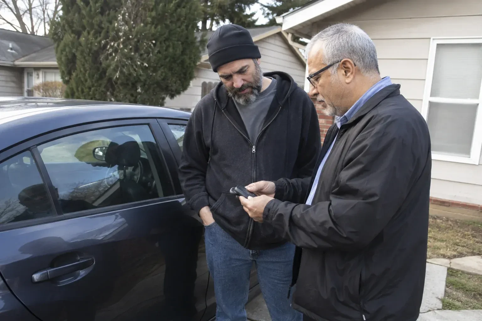 Two adults discussing a key fob beside a parked car. — Car Lockout Service, Brantford
